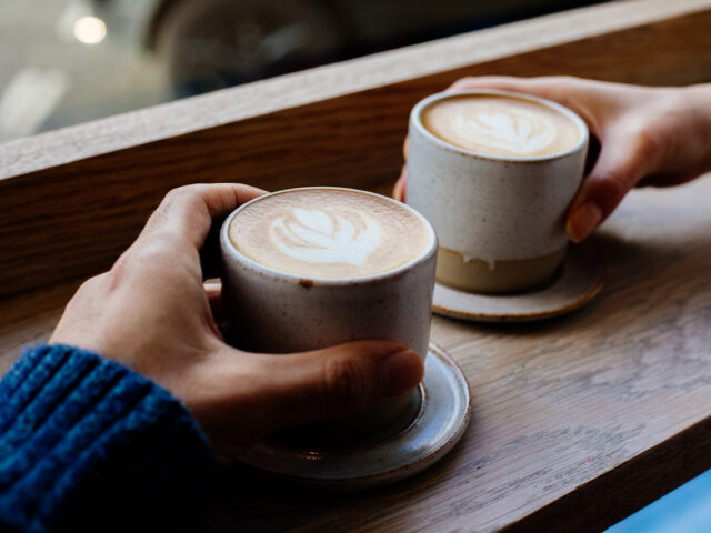 Close up woman and man holding cups of coffee on table: coffee audio campaign